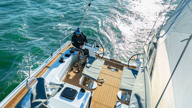 Aerial view of someone steering the Hanse 410 with the sun on the water. The person is wearing warm clothes.