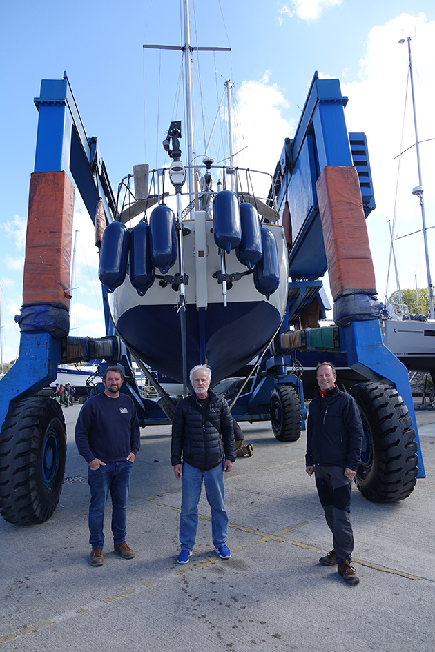 Three men standing in front of a boat in a craddle