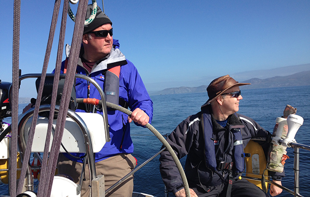 A man helming, while the skipper looks out to sea