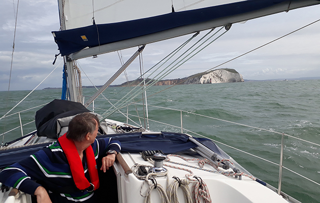 A skipper wearing a red lifejacket looking towards land from the cockpit of a yacht
