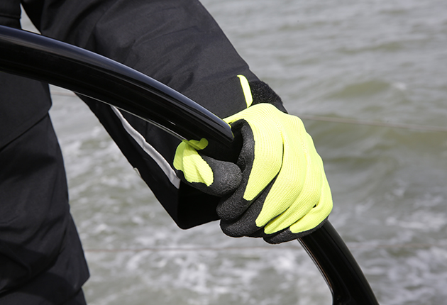 A person wearing black and yellow Musto dipped gloves while sailing
