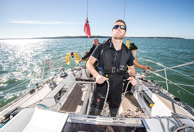 A crew member wearing sunglasses checks the spinnaker on a yacht