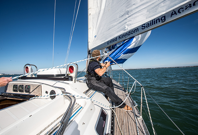 A crew sitting on the deck of a yacht adjusting guys