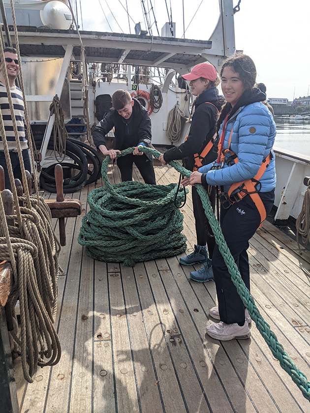 Children holding rope and coiling it on the deck of a large ship