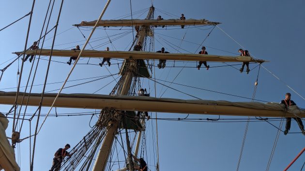 Crew up the rigging on a tall ship preparing to drop the sails