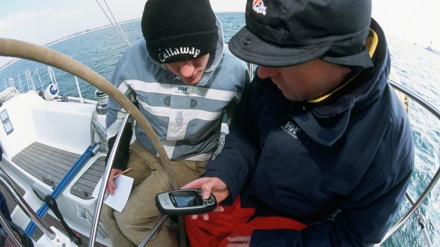 Two men using a digital handheld plotter on a yacht