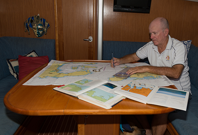 A man sitting at a table looking at charts on a yacht