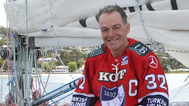 A man waring a red shirt sitting on the deck of a yacht