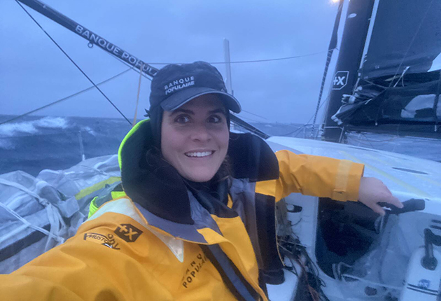 A female skipper wearing wet weather gear on the deck of an IMOCA 60 during the Vendee GLobe