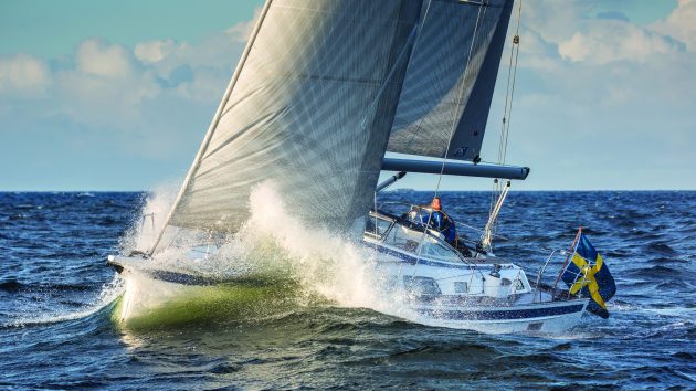 A yacht sailing through waves flying a Swedish flag