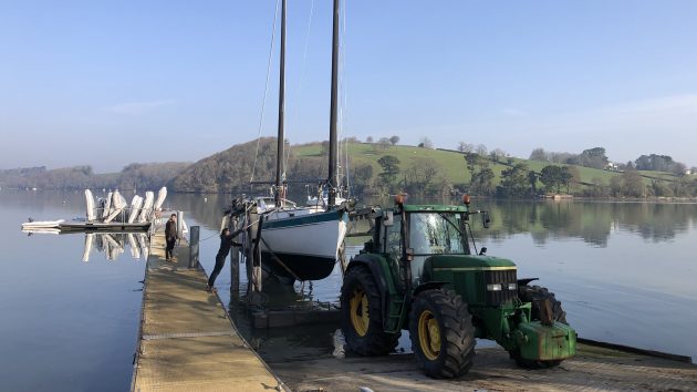 A boat with two masts being towed out of the water with a tractor