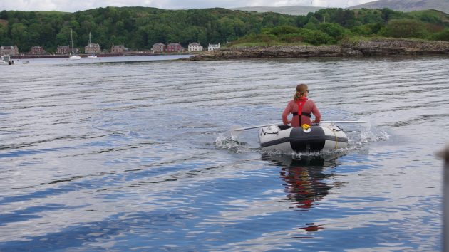 A woman wearing a red jumper and a red lifejacket rowing a dinghy
