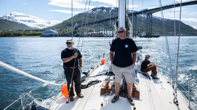 Men standing on the deck of a yacht wearing shorts and tshirts