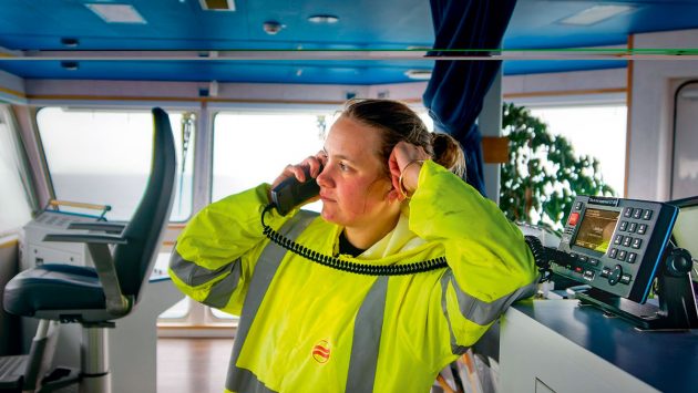 Marine satellite communication: A woman wearing yellow hi-viz on a phone on the bridge of a ship