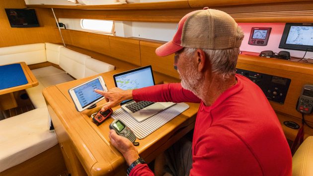 A sailor wearing a baseball cat looking at weather data on a computer screen while sailing