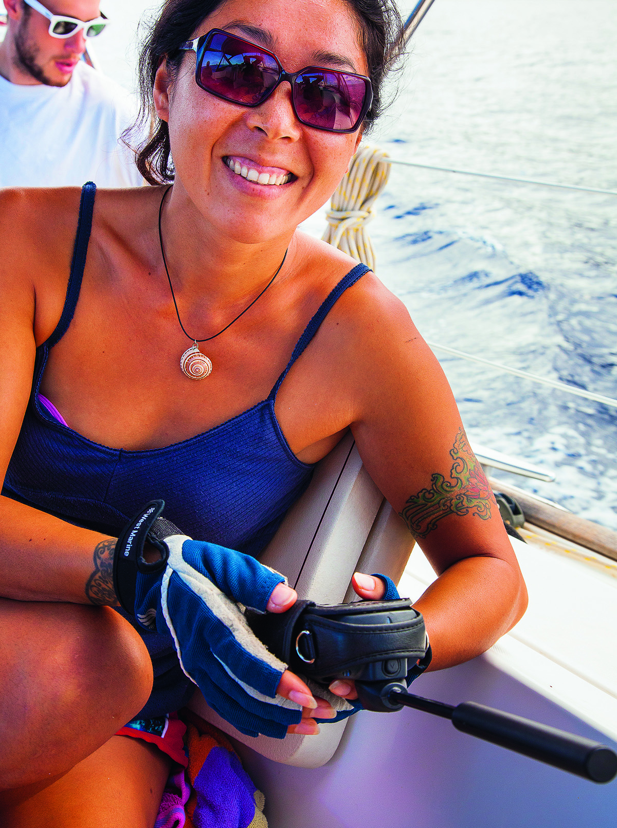 A woman wearing sunglasses and a tshirt holding a black sat phone on a boat