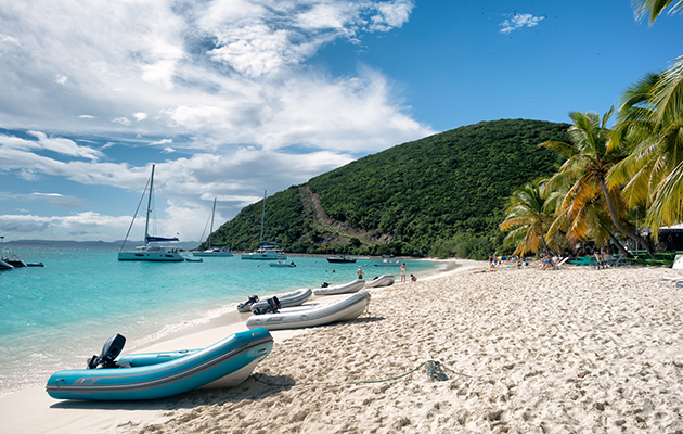 Cruising After Brexit-Dinghies on a beach with catamarans and multihulls anchored in the bay