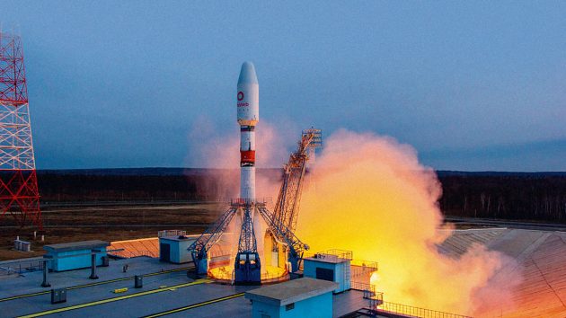 A rocket taking off with white and orange smoke carrying satellites