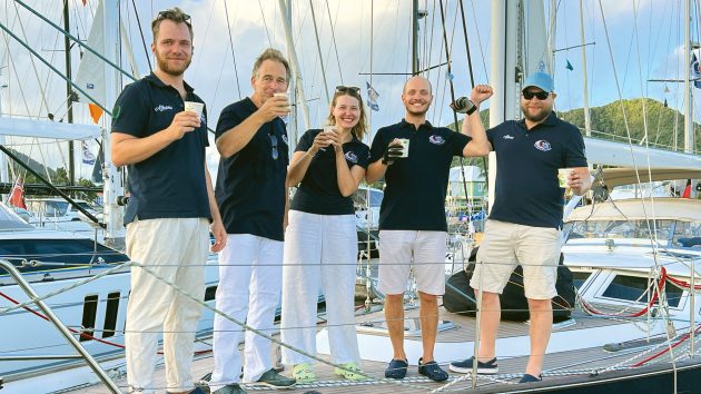 The five crew members in matching navy t-shirts celebrating with drinks aboard.