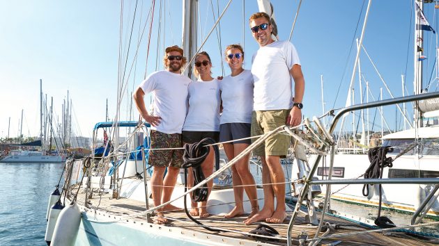 Phoebe, Tom, Millie, and David in t-shirts and shorts aboard the boat. There are no clouds in the sky.