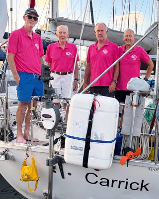 The crew are wearing matching pink t-shirts and standing aboard the Carrick. The sun is setting behind them.