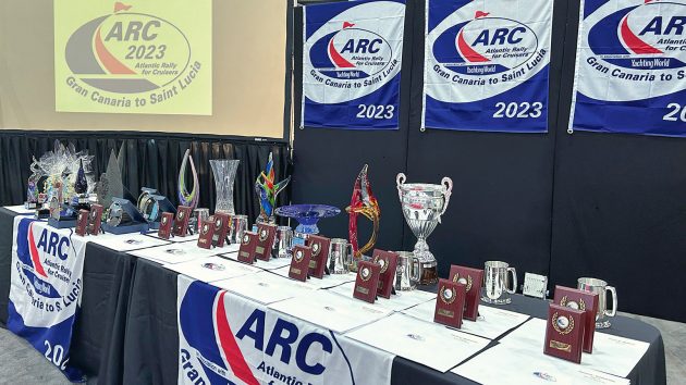 A table with various cups and wooden awards lying. There are ARC banners around these awards.