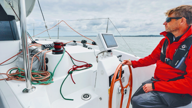 Theo at the helm in a red coat and life jacket